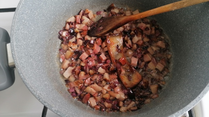 1. Na olivovom oleji smažíme na kocky nakrájanú cibuľu, osolíme, po chvíľke pridáme aj slaninku a smažíme do zlatista. Pokojne tam hoďte aj kožu a ponechajte počas celej doby varenia omáčky, pustí skvelú chuť.
