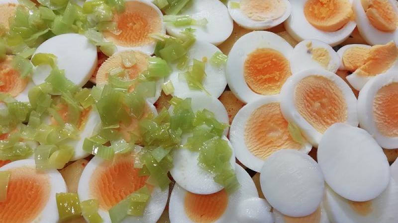 2. Zemiaky okoreníme (soľ, čierne korenie, červená paprika, kurkuma, rasca). Ošúpané vajcia prekrojíme na kolieska, poukladáme ich na pripravené zemiaky. Pór nakrájame na malé kocky, orestujeme na polievkovej lyžici masla.