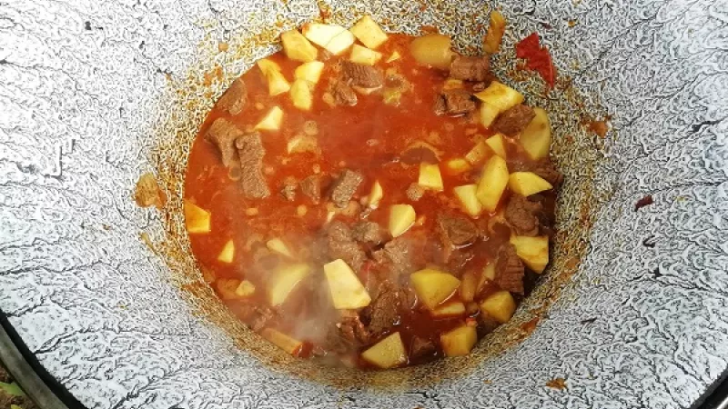 6. Pripravenú zeleninu pridáme k duseniu mäsa. Zemiaky ošúpeme, umyjeme a nakrájame na kocky. Keď je mäso polomäkké, tak ich tiež pridáme. Pridáme aj roztlačený cesnak, feferónku podľa chuti.