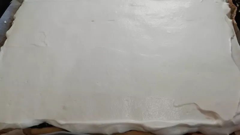 14. Vyšľahanú šľahačku, ktorú sme si rozotreli, zarovnáme po celej ploche koláča. Čokoládu nastrúhame.