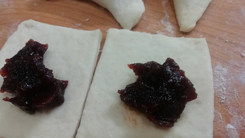 3. Tvarohové cesto rozdelíme na dve časti. Každé rozvaľkáme na hrúbku 3 mm, pomáhame si ďalšou múkou, aby sa nelepilo. Cesto nakrájame na štvorčeky veľkosti 6x6 cm, dáme náplň, preložíme, dobre zatlačíme.
