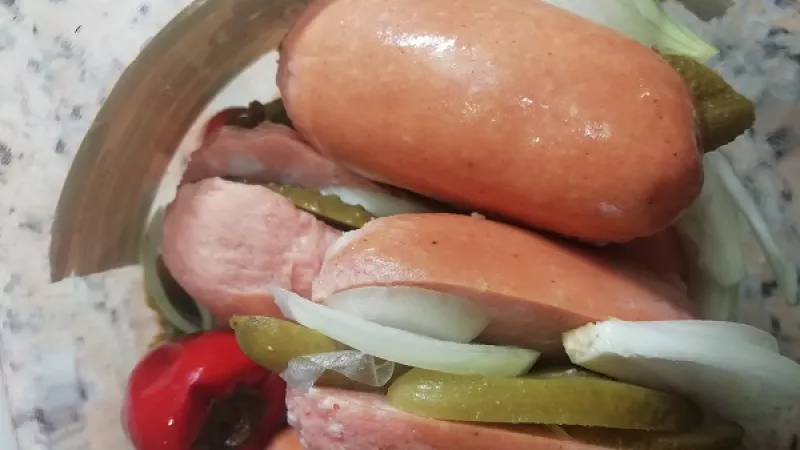 3. Sklo si dôkladne umyjeme a osušíme. Ak nemáme 4 l sklo, môžeme zvoliť aj menšie poháre. Kyslé uhorky a cibule nakrájame na tenké plátky. Do skla postupne ukladáme naplnené špekáčky, ktoré prekladáme ďalšími plátkami uhorky, cibule a celými feferónkami. 